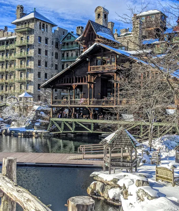 Cozy Winter Weekend Getaways from New York - A older wood and brick style building is pictured on the edge of some water. It is snowy and there are people on the various porches of the building.' title='The 34 Coziest Winter Weekend Getaways from NYC in 2025