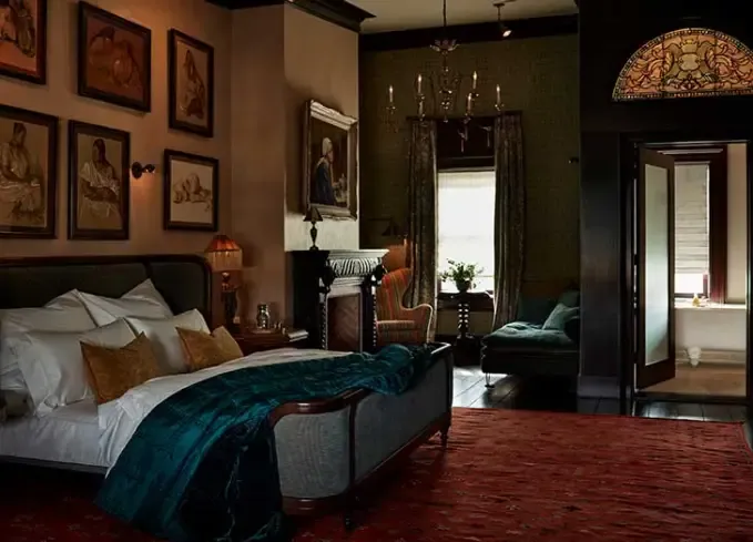 Cozy Winter Weekend Getaways from New York - A large bed with a teal blanket sits in a dim room at The Maker. The walls are covered in paintings and the room is dark and cozy.' title='The 34 Coziest Winter Weekend Getaways from NYC in 2025