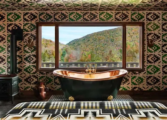 Cozy Winter Weekend Getaways from New York - A copper and patina bathtub sits in front of a massive window overlooking the foliage. The interior of the room features geometric patterns on the floor and walls.' title='The 34 Coziest Winter Weekend Getaways from NYC in 2025