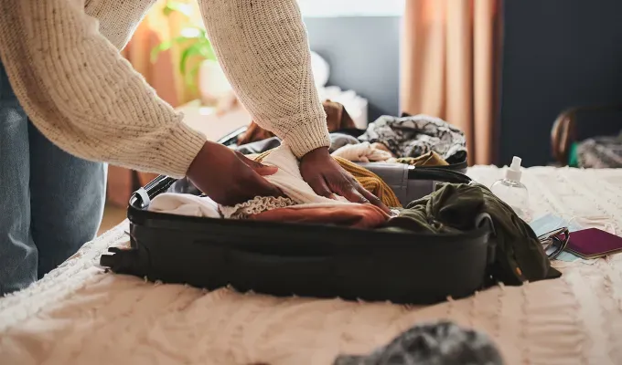 International Travel Packing List Carry-On Bag Restrictions: person packing their things into a carry-on suitcase' fetchpriority='auto' title='Your Ultimate International Travel Packing List for a Stress-Free Trip (Plus What to Bring and Helpful Packing Tips)