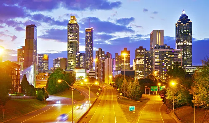 father-son-trip-ideas: The bright city lights of Atlanta at night. The photo is of the skyline at night taken from above a highway. The sky is blue and purple with clouds.' title='10 Father-Son Trip Ideas for Some Serious Bonding
