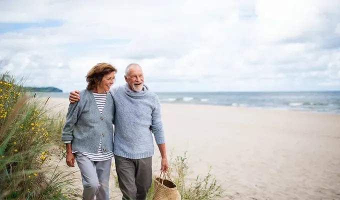 What Might Happen If You Stop Drinking Soda - A smiling older couple walk along the back edge of a beach near the dunes.' fetchpriority='auto' title='8 Things That Might Happen If You Stop Drinking Soda