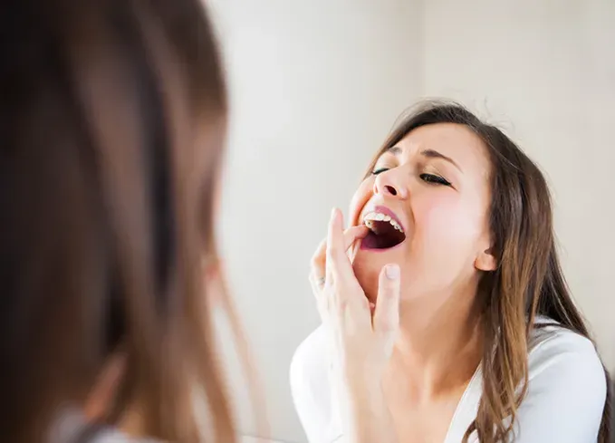 woman looking at teeth in mirror' fetchpriority='auto' title='What Does It Mean When You Dream About Your Teeth Falling Out or Breaking?